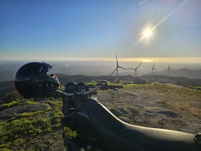 Sole basso sopra una moto e pale eoliche lontane tra le colline.