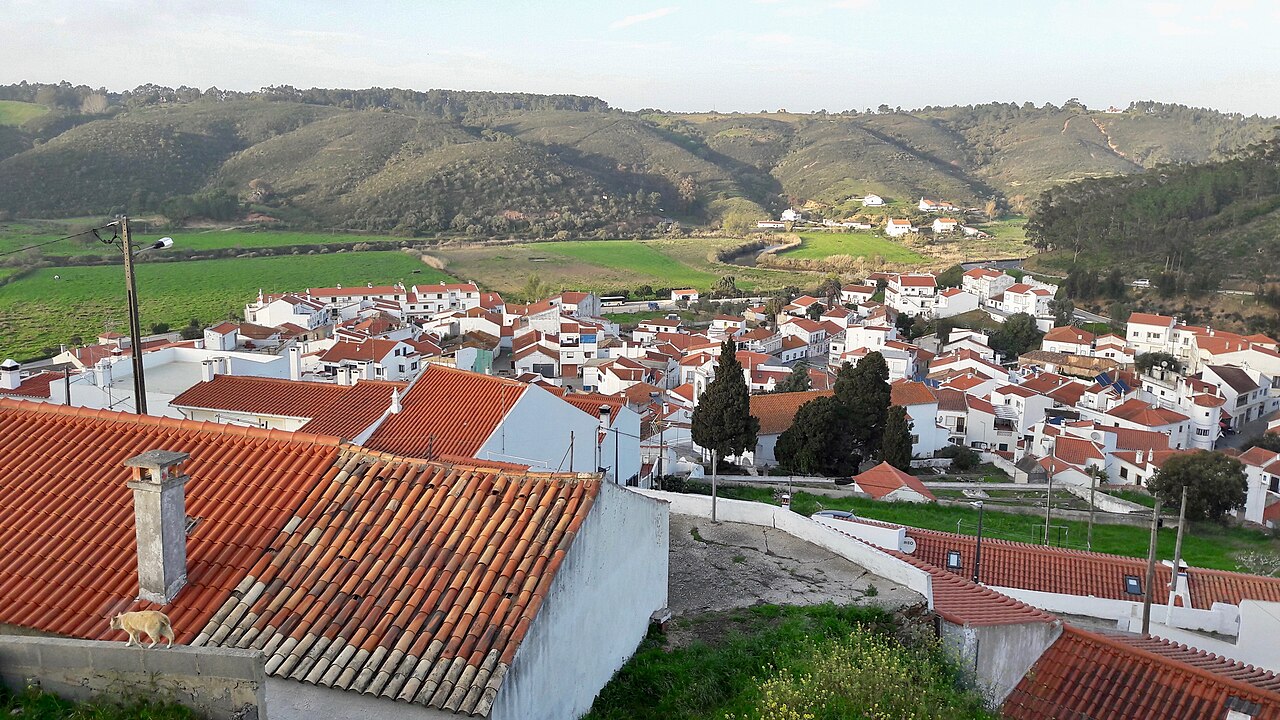 Red tiled roofs and white houses in Odeceixe, with green hills behind.