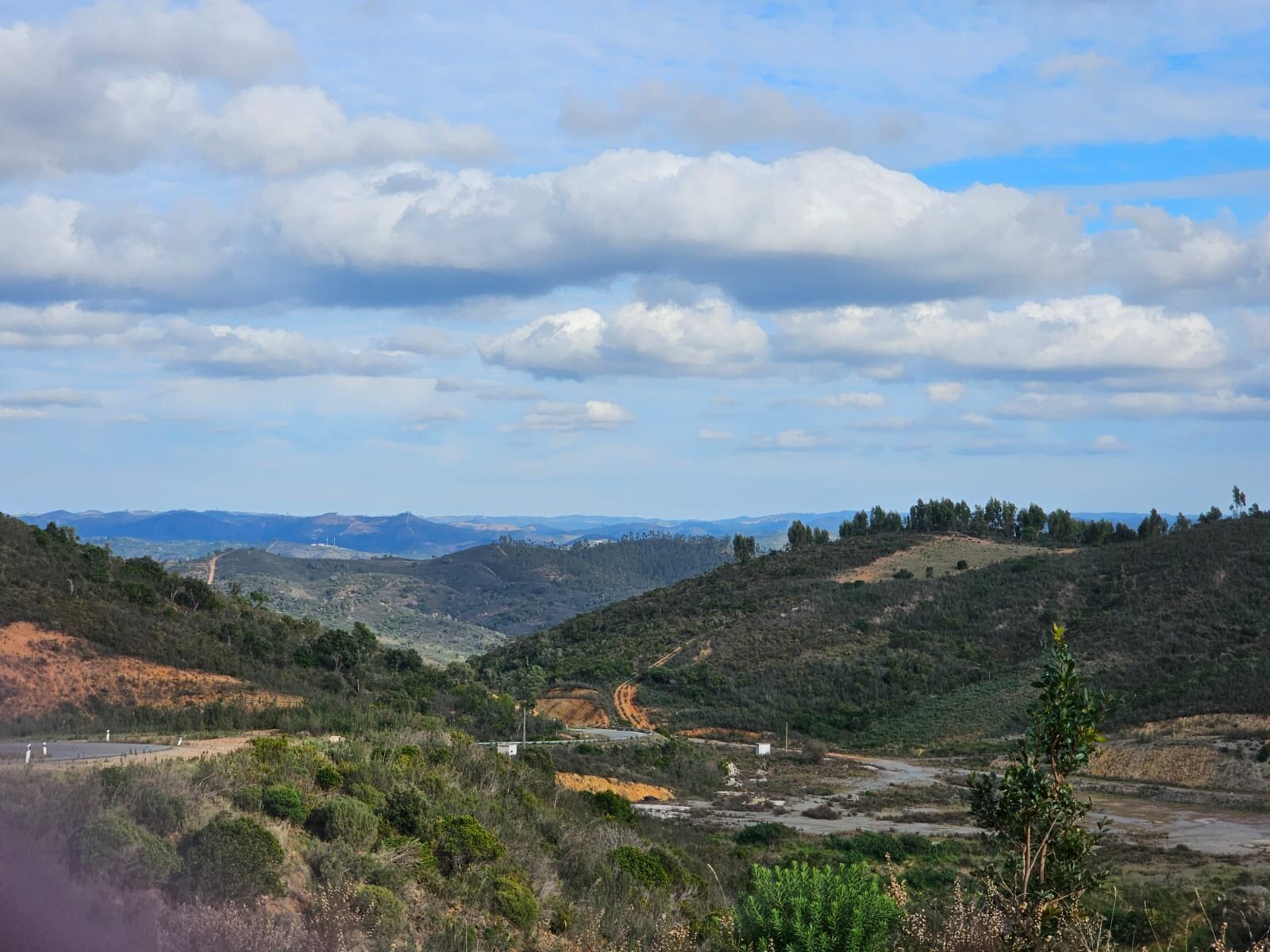 Rolling Algarve hills and winding dirt tracks beneath a cloudy blue sky