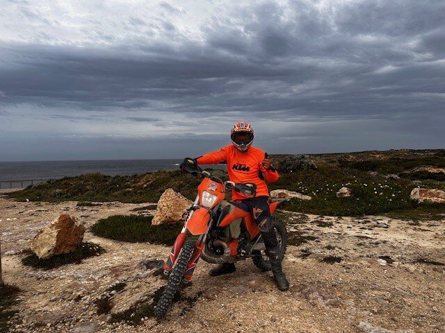 A rider on an orange KTM motorcycle beside the Algarve coast